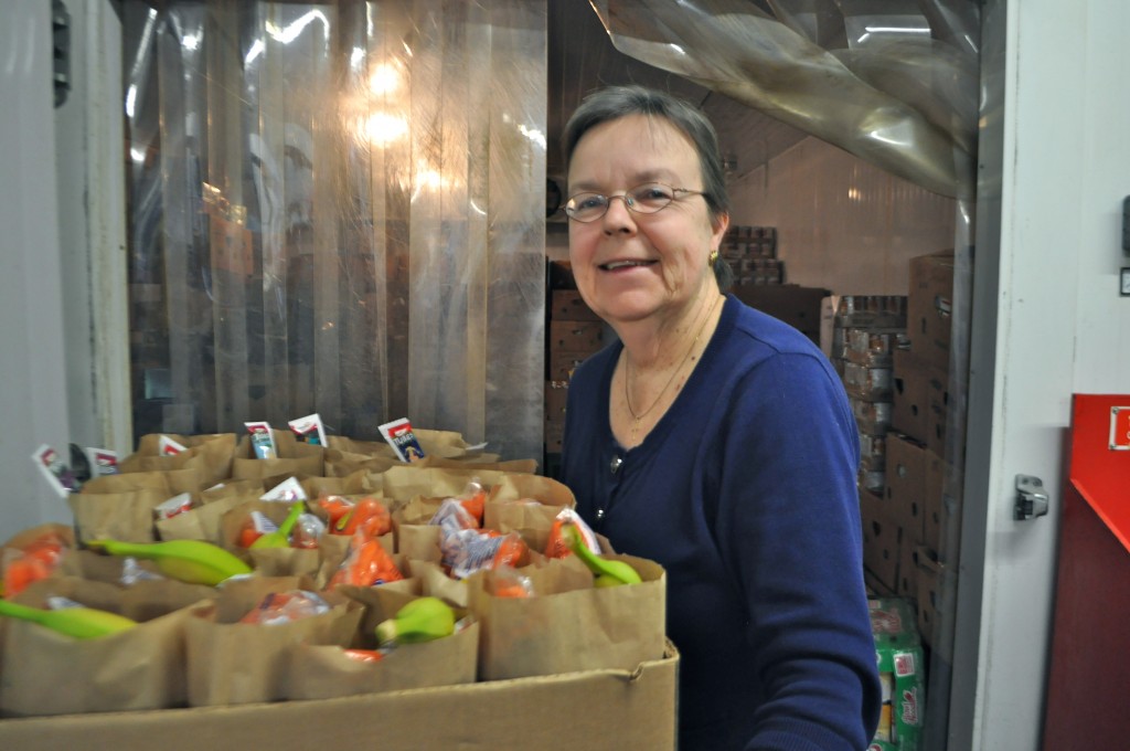 Christine Hager, executive director of the Sharing Place food bank, is pictured with brown bags full of healthy lunch items for school-age children. 